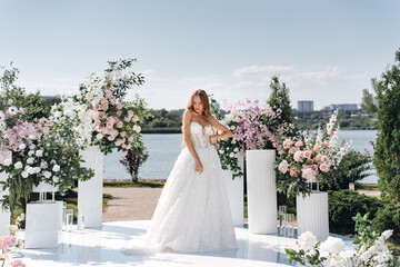 A bride in a wedding ceremony area decorated with flowers on the riverbank. 
