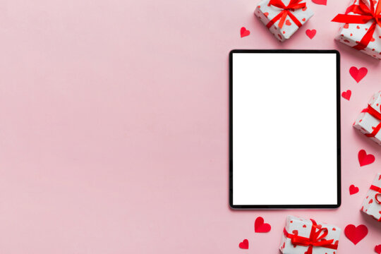 Top view of digital tablet with gift boxes and hearts on colorful background. Tablet with black screen with Holiday decorations gift box top view