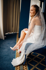 The bride in simple beautiful elegant wedding dress puts on shoes