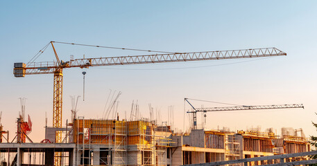 Cranes overseeing a new building site, indicating urban growth and real estate development. Modern apartments are under construction © EdNurg