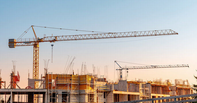 Cranes overseeing a new building site, indicating urban growth and real estate development. Modern apartments are under construction