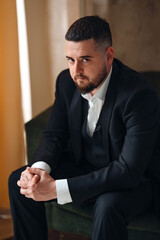 A serious, thoughtful man in a business suit is sitting in an armchair.