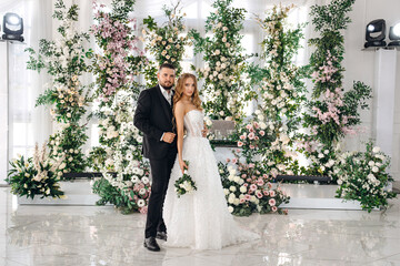 newlyweds embrace in a room decorated with many flowers
