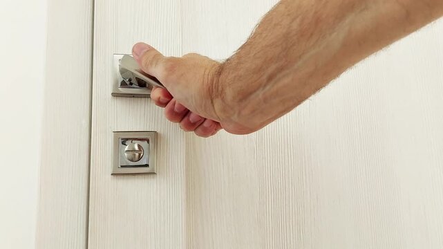A hand smoothly closes a modern door with a brushed metal handle. The motion is clean and deliberate, highlighting the handles texture and the doors sleek surface