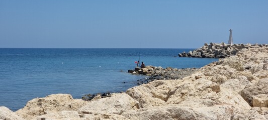 Peaceful Rocky Coastline with Fishermen and Breakwater