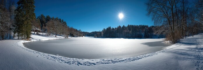A panoramic view of a frozen lake under a bright sun, with snow-covered banks and trees silhouetted against a clear blue sky