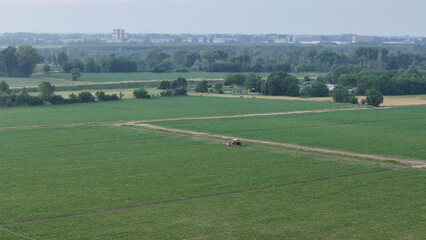 Aerial perspective of a farmer operating a tractor applying crop protection products to a lush green soybean field in the countryside near Piacenza Italy showcasing advanced farming techniques