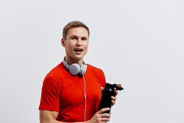 smiling young caucasian man wearing red t-shirt holding shaker bottle headphones around neck studio...