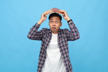 Emotional and shocked young asian man wearing casual clothes with open book on his head, looking...