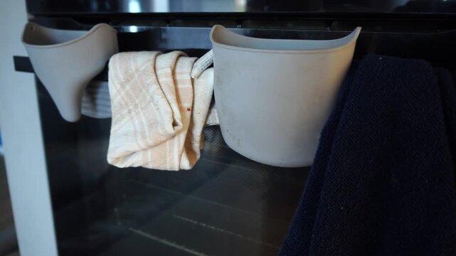 Practical kitchen organization with gray silicone caddies and folded towels hanging neatly on a modern oven door handle