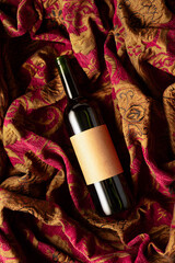 Bottle of red wine on a retro tapestry with dark red and golden floral ornament.