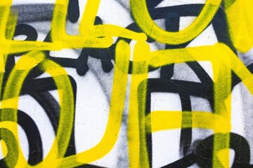 Naklejka premium Bold graffiti pattern in yellow, black on white wall. Urban street art, vibrant, funky, abstract lines. Creative backgrounds, modern 90s, 2000s, digital art inspiration, city visuals.