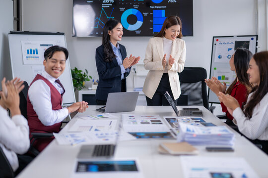 Business team clapping in meeting celebrating success with charts and graphs