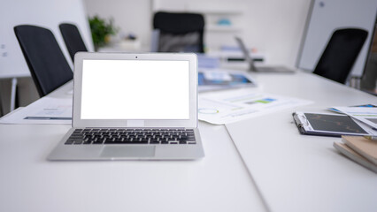 Laptop showing blank screen sitting on meeting room table with scattered documents