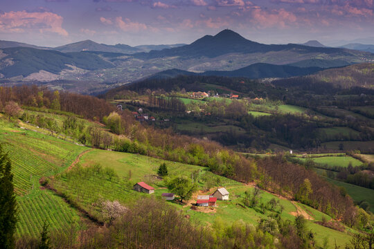 Lush hills and valleys bask in the warm sunlight, with a picturesque village nestled amidst the stunning scenery and majestic mountains in Serbia