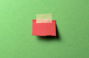 Cut out torn piece of red paper note with rough texture edges and adhesive tape with copy space for text on green background