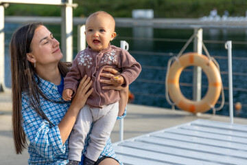 Mother lifting baby on pier by the water. Warm family moment