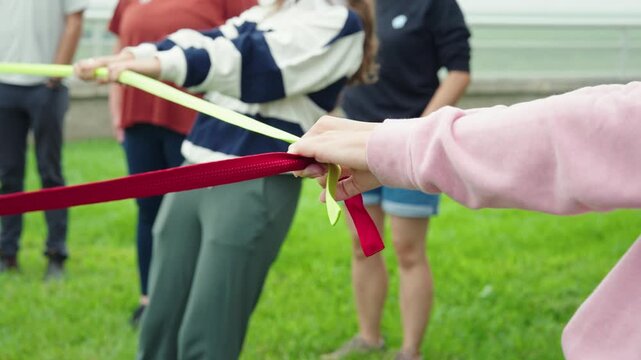 Close up shows woman gripping red strap in circle for outdoor group activity