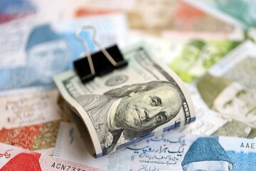 Roll of US dollar bills lies on big amount of Pakistan rupees banknotes close up