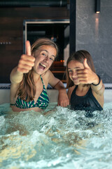Two girls in jacuzzi with thumbs up, laughter and splashes. Family spa chill.