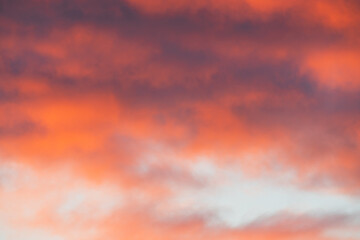 Dreamy soft-focus abstract background of a vibrant sunset sky with painterly orange, red, and purple clouds.