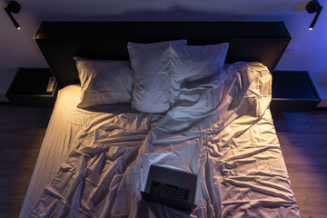 Overhead view of bed with lit laptop and contrast light. Night work.