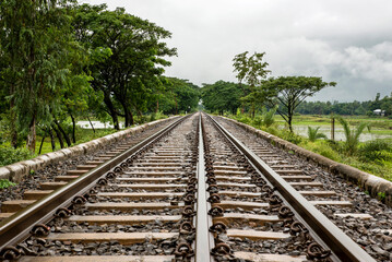 Obraz premium Long Railway Tracks Stretching Into the Distance Through Green Countryside Under Cloudy Sky