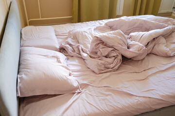Side view of an unmade bed with pink sheets, pillows, and blanket in morning light, showing realistic home life after waking up