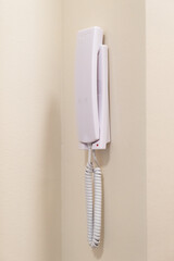 Close-up of a modern white intercom handset mounted on a wall near apartment entrance. Communication and security system detail