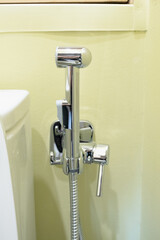 Close-up view of a modern chrome steel hygienic shower installed near toilet. Personal hygiene and bathroom sanitation concept