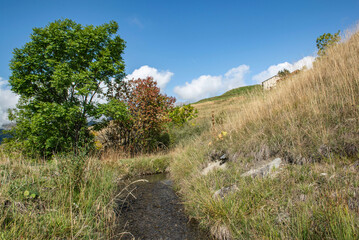 rural landscape crossed by a small stream through the fields and the hills under blue sky