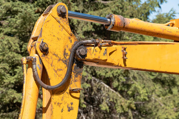 Yellow excavator arm featuring a hydraulic piston and cylinder, showing wear and tear from heavy industrial use in a natural outdoor setting