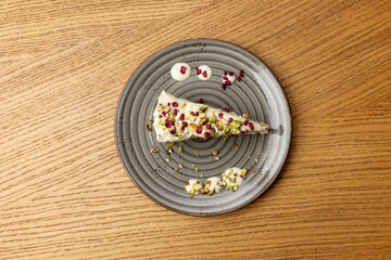 Top view of a slice of cake with white icing, pistachios, and pomegranate on a plate