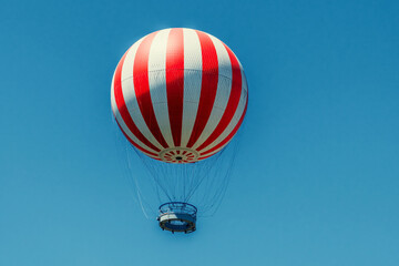 Obraz premium A vibrant red and white striped hot air balloon floats serenely against a clear, bright blue sky