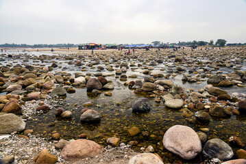 People Exploring A Rocky Riverbed With Large Boulders Under Mountain Ridge