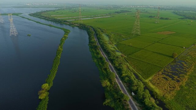 Aerial drone shot wide panning shot over lush green monsoon farms and a water body crossed by power lines, early sunrise atmosphere near Delhi, India.