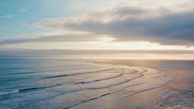 Sunrise on ocean coastline with gentle waves rolling in and reflecting sky colors.