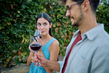 Young couple enjoying a romantic wine tasting experience outdoors in a vineyard, smelling the aroma of red wine