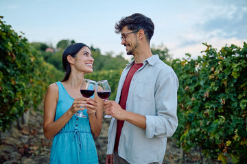 Happy couple clinking red wine glasses, enjoying tasting at a beautiful vineyard during a romantic outdoor date