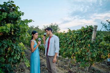 Young couple enjoying a romantic wine tasting experience outdoors in a beautiful vineyard. They are evaluating aroma and color