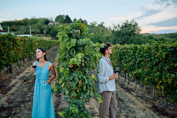 Young couple standing in a vineyard, tasting red wine during an outdoor date, enjoying a beautiful nature setting