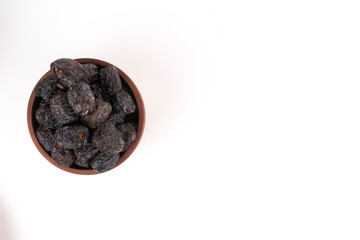 A top down view of a brown bowl filled with dark, dry dates is placed on a white background.