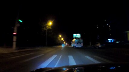 Nighttime driving at black car overtaking another vehicle on a well-lit road, with illuminated billboards and streetlights enhancing the dynamic motion and atmosphere of the scene