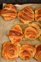 A detailed top-down view of a baking sheet filled with freshly baked, golden croissants and spiral pastries