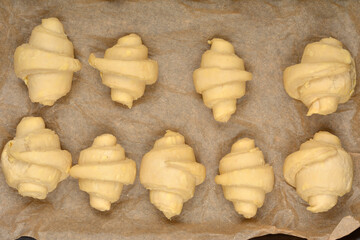 An overhead close-up of raw, rolled croissant dough pieces arranged on parchment paper before baking
