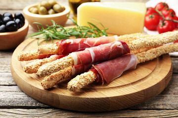 Delicious grissini sticks with sesame seeds and prosciutto on wooden table, closeup