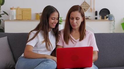 Young teenage student girl sitting on sofa at home with her mid adult mother, both sharing time together while using laptop computer. Family and technology lifestyle concept - Powered by Adobe