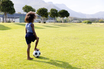Obraz premium African American girl in sportswear standing barefoot on sports field resting foot on soccer ball