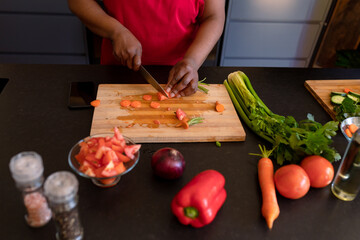 African American mature woman in red shirt slicing carrots on cutting board at kitchen counter