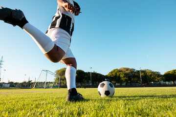 African American man kicking soccer ball on field wearing striped jersey and cleats, copy space